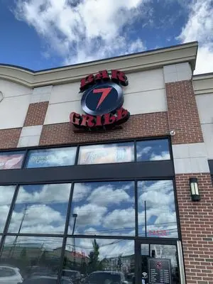 Exterior of a Bar 7 Grill storefront with red-and-black sign above glass windows under a cloudy sky