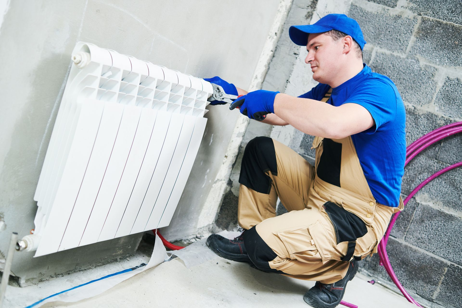A man is kneeling down fixing a radiator with a wrench.