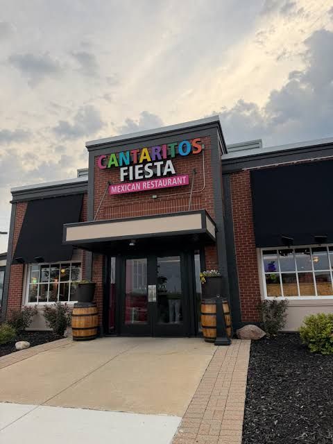 Entrance to a Cantartitos Fiesta restaurant with black awning, brick facade, and cloudy sky