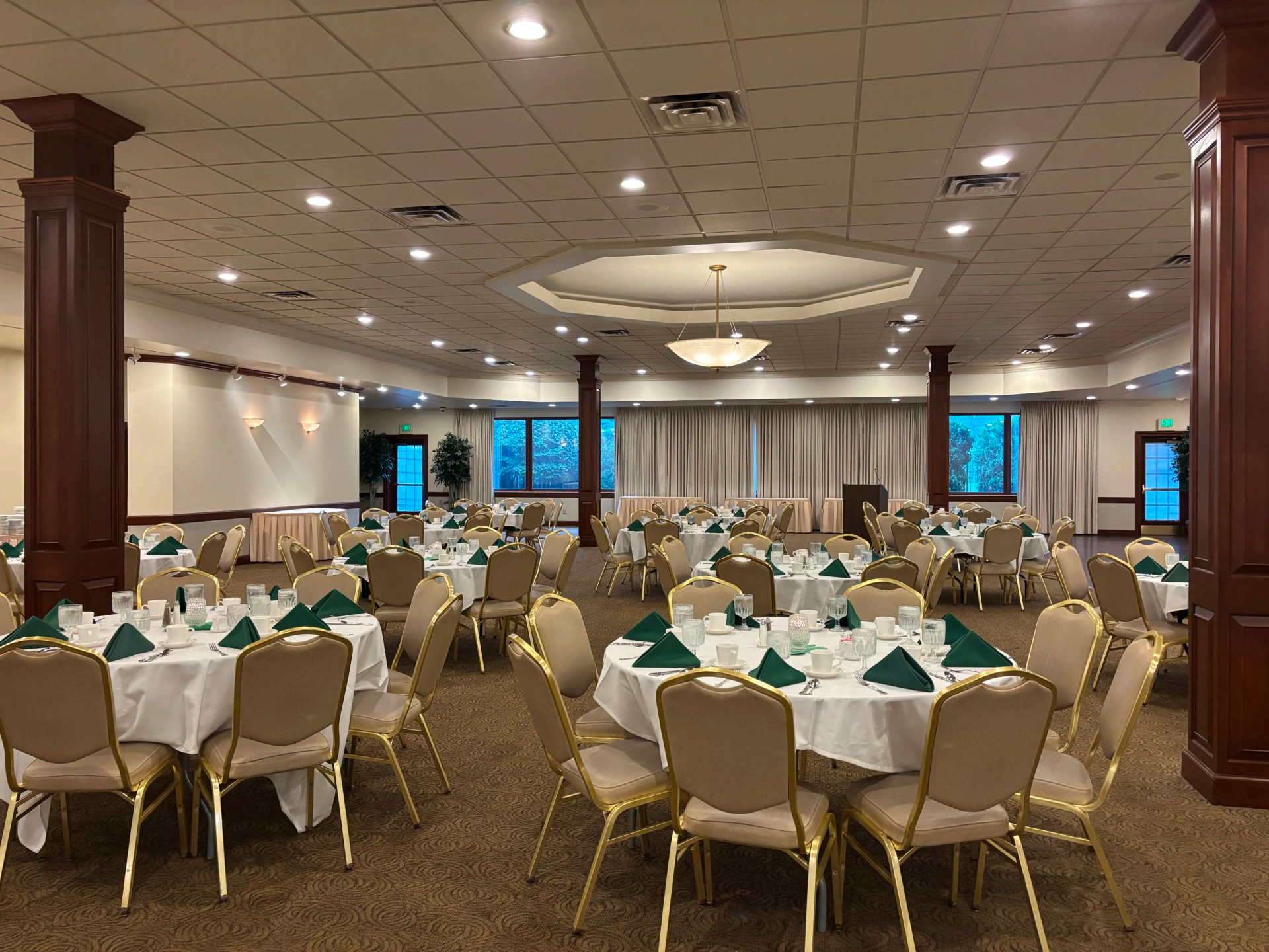 Empty park place banquet hall set for a formal dinner, with round tables, beige chairs, and green napkins