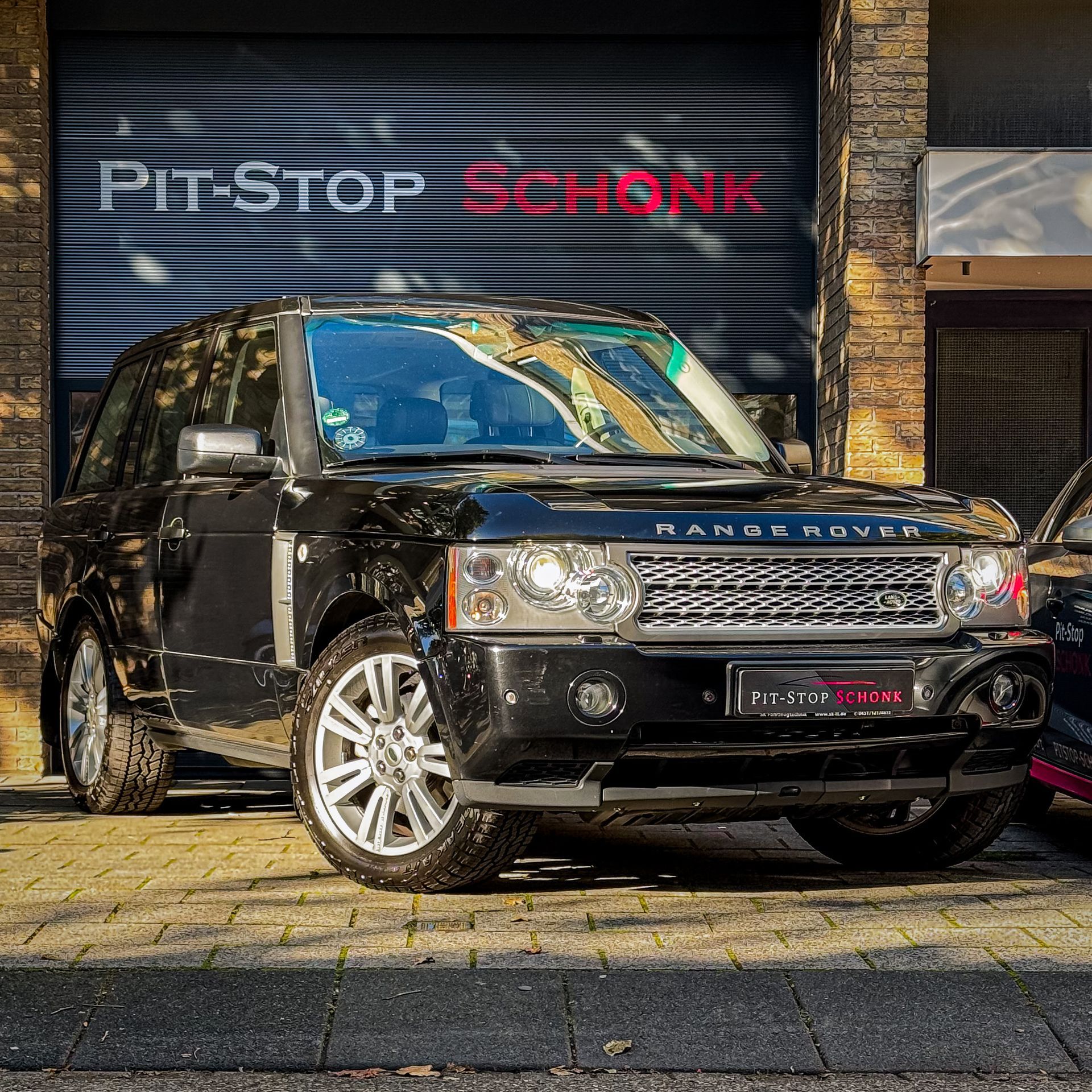 Een zwarte Range Rover staat geparkeerd voor een garagedeur.