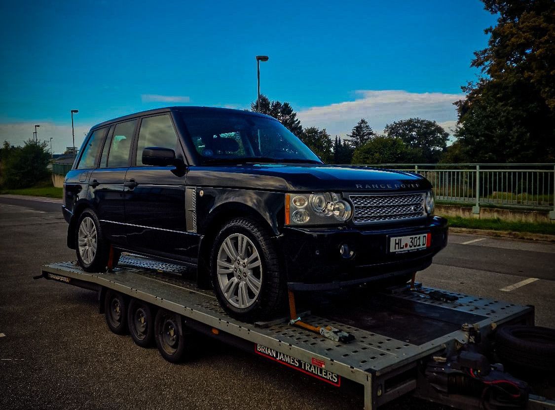 Een zwarte Range Rover staat op een aanhanger op een parkeerplaats