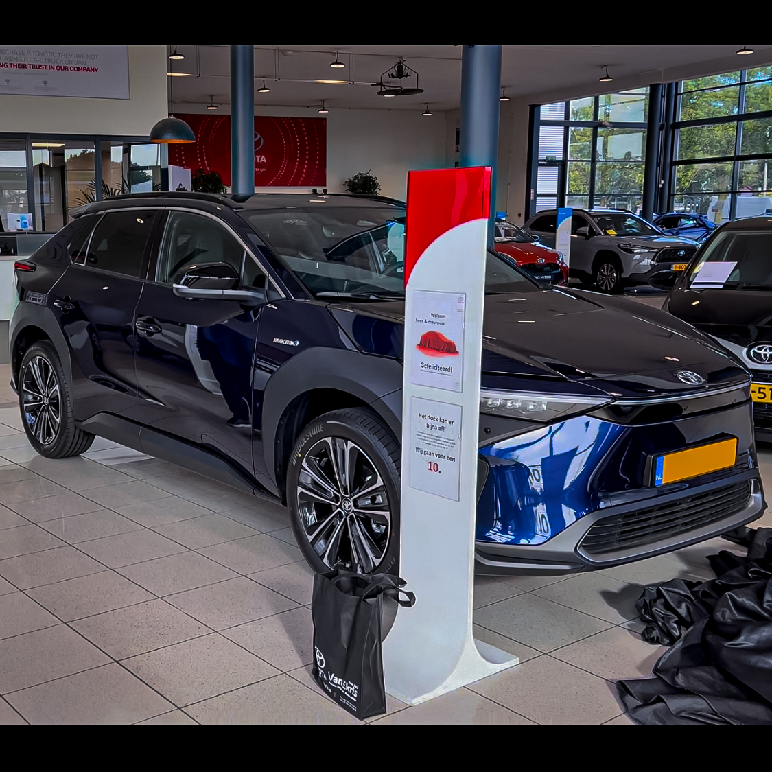 Een blauwe auto staat geparkeerd in een showroom naast een bord.