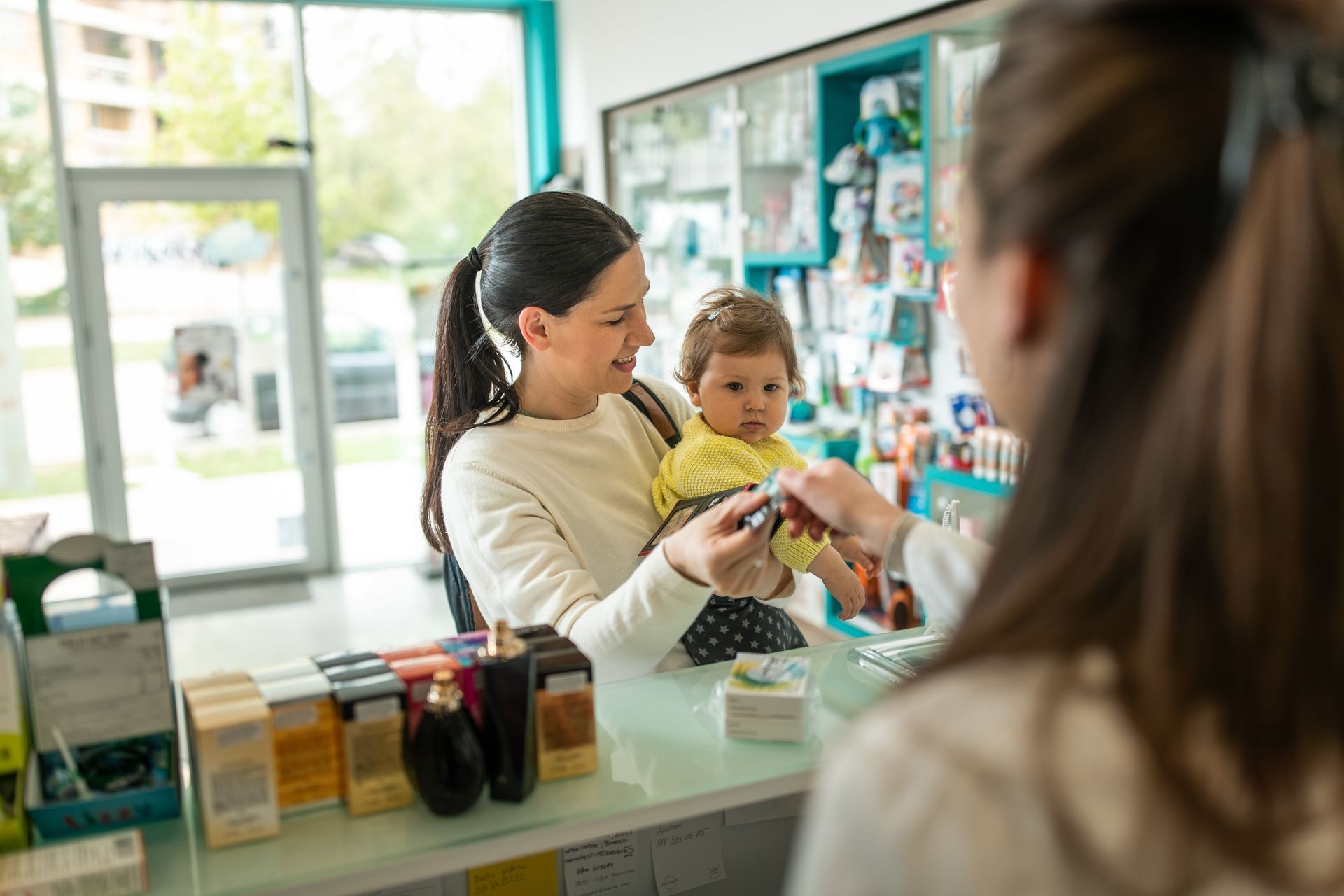 Una donna tiene in braccio un bambino mentre è in piedi al bancone di una farmacia.
