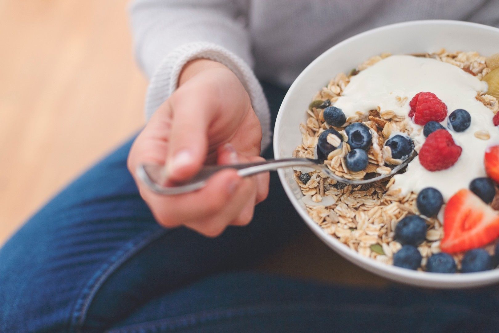 Una persona sta mangiando una ciotola di cereali con yogurt e frutti di bosco.