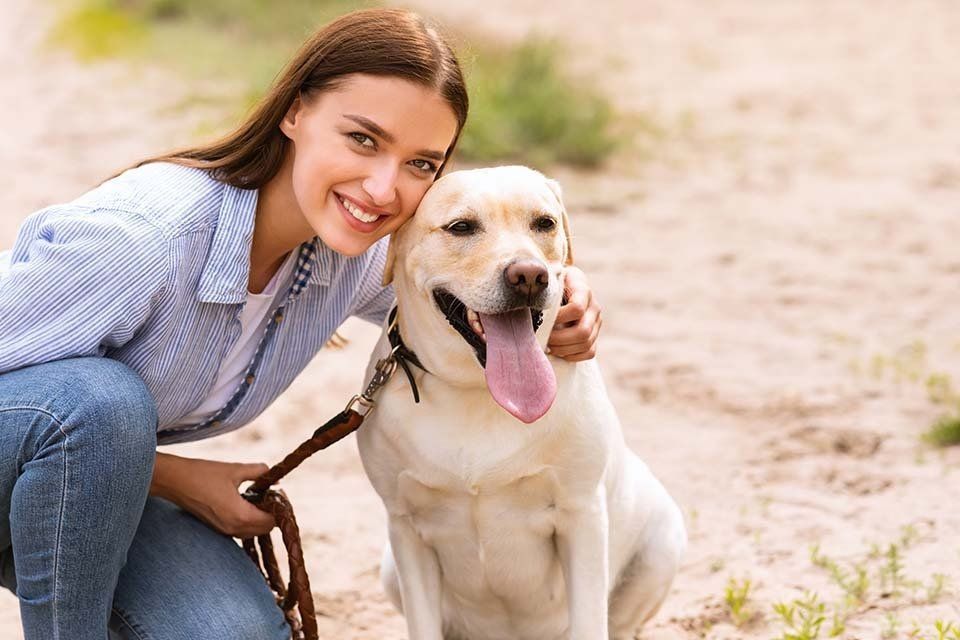 Una donna è inginocchiata accanto a un cane al guinzaglio.