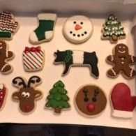 Assorted decorated Christmas cookies arranged on a tray, including stockings, snowman, cow, gingerbread man, and tree.