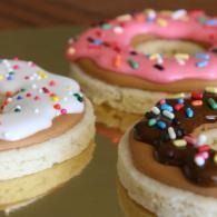 Three decorated donuts with white, pink, and chocolate icing and colorful sprinkles on a tray