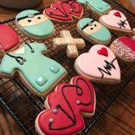 Decorated heart and medical-themed cookies on a cooling rack, in pink, teal, and white.