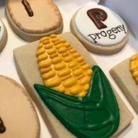 Decorated cookies shaped like corn cobs and a round logo cookie with the word “Progeny”