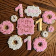 Pink donut-shaped birthday dessert arrangement with “Happy Birthday Blaire!” and the number 1 on a wooden table