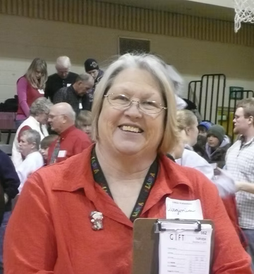 Woman in red shirt smiles, holding clipboard. Others in background.