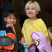 Two smiling children with backpacks, one blond and one with dark hair.