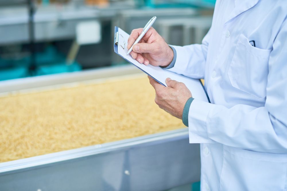 Technician in white coat taking notes beside a food processing conveyor line