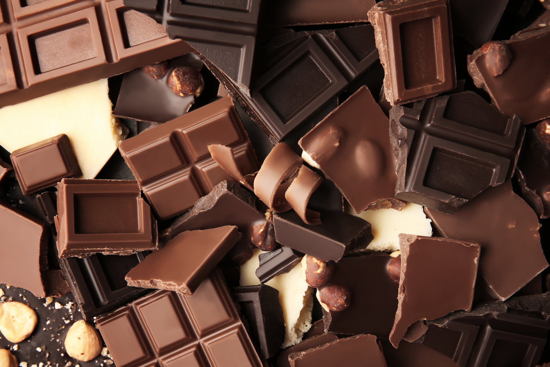 Assorted milk and dark chocolate pieces piled together, with a few nuts visible