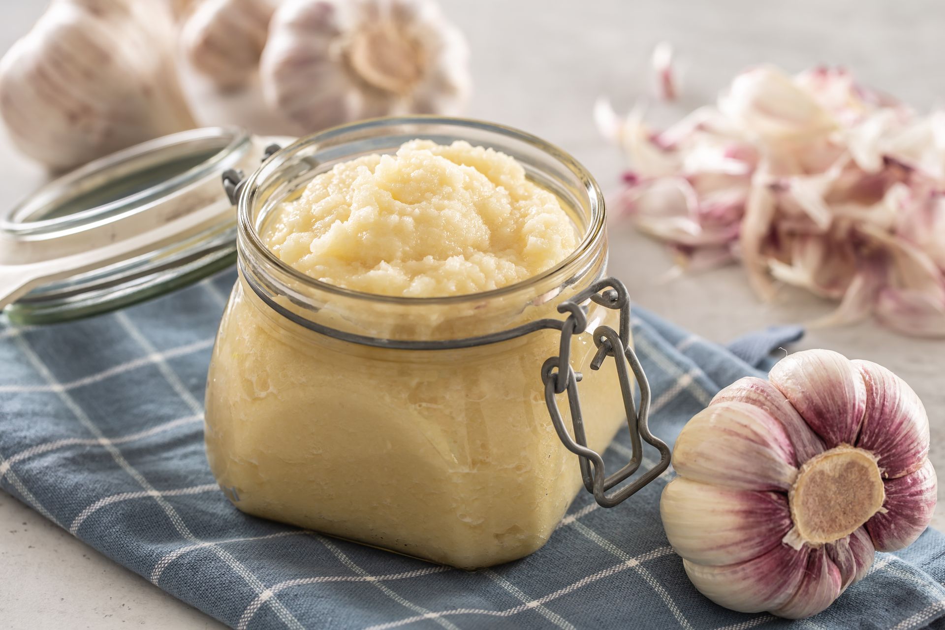 Jar of whipped garlic butter on a blue cloth with garlic bulbs nearby