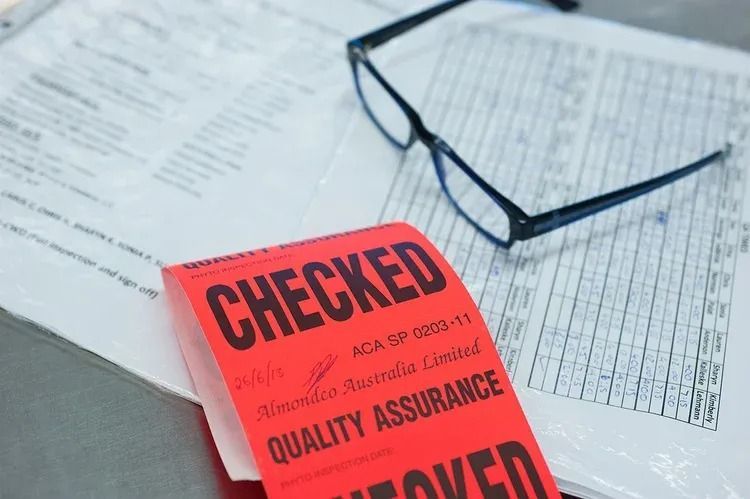 Red checked quality assurance stamp on paperwork beside black eyeglasses