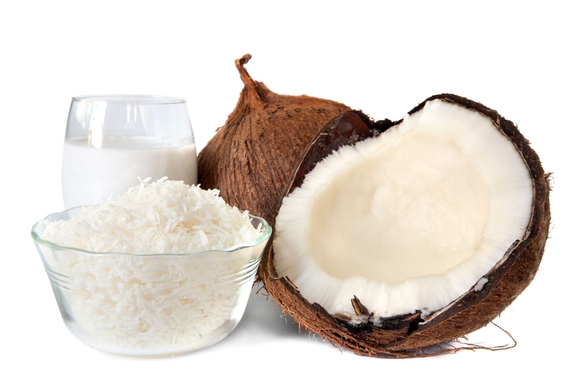 Coconut milk, shredded coconut, and halved coconuts on a white background