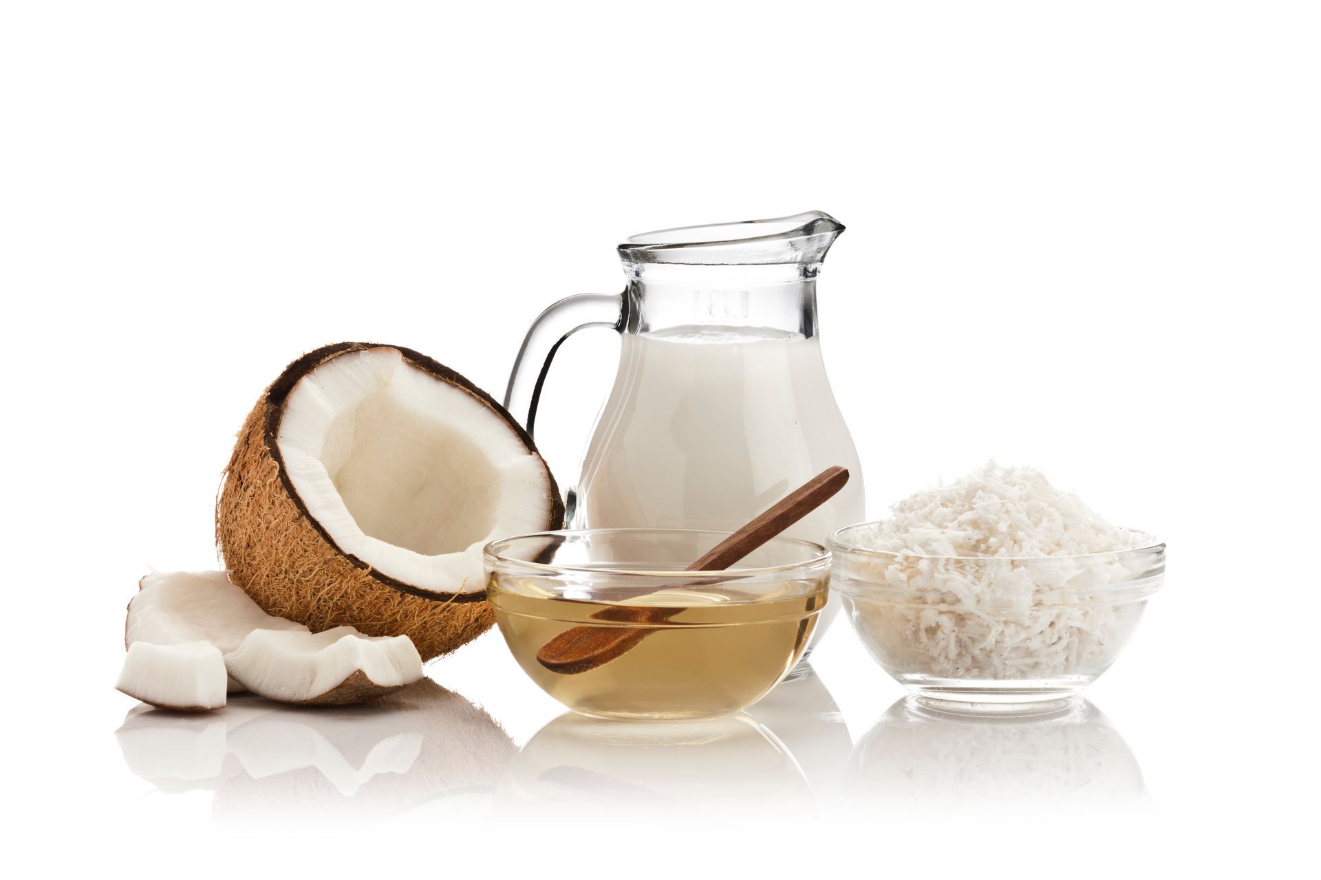 Coconut oil, half coconut, milk pitcher, spoon, and shredded coconut on a white background