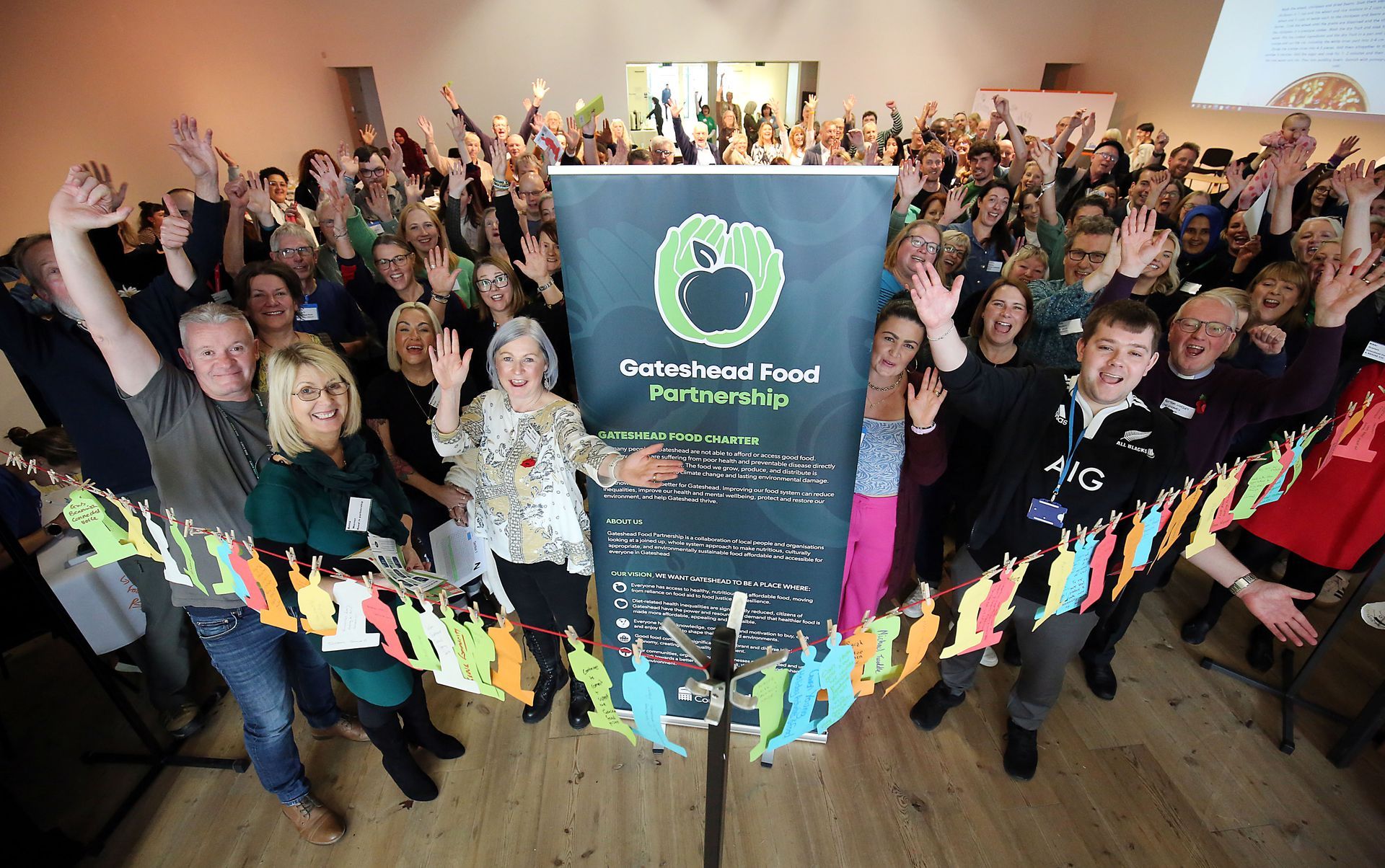 A large group of people are posing in front of a sign that says tree of goodness