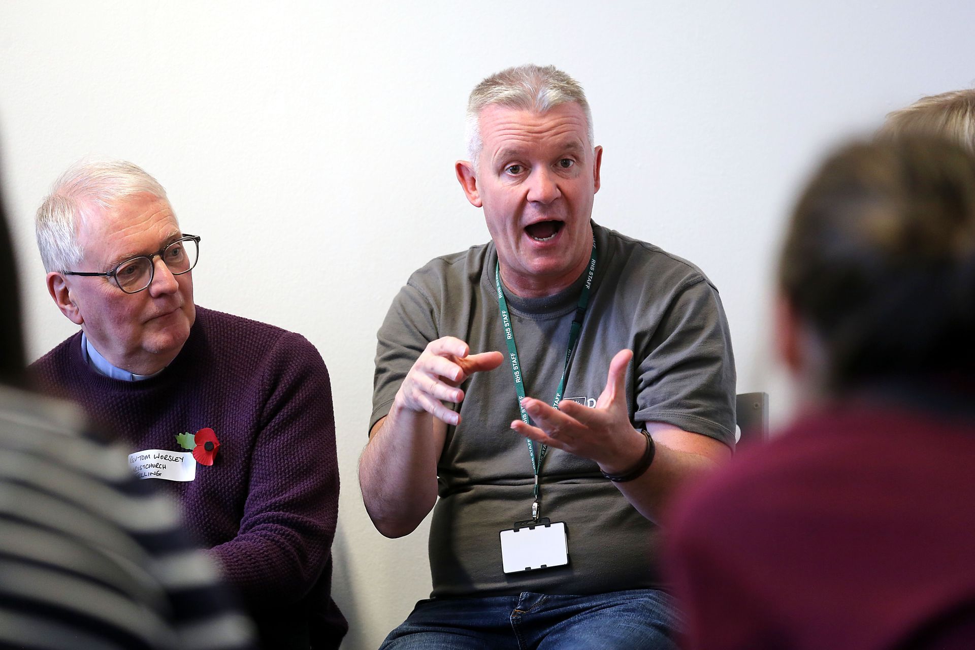 Two people seated in discussion, one speaking and gesturing in a meeting room.