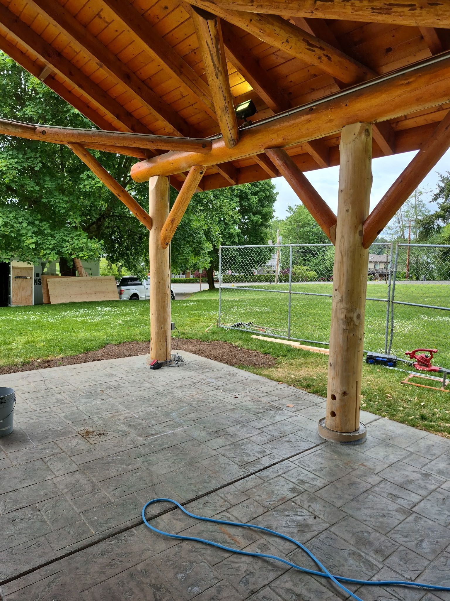 Wooden gazebo with concrete floor, green lawn in background.
