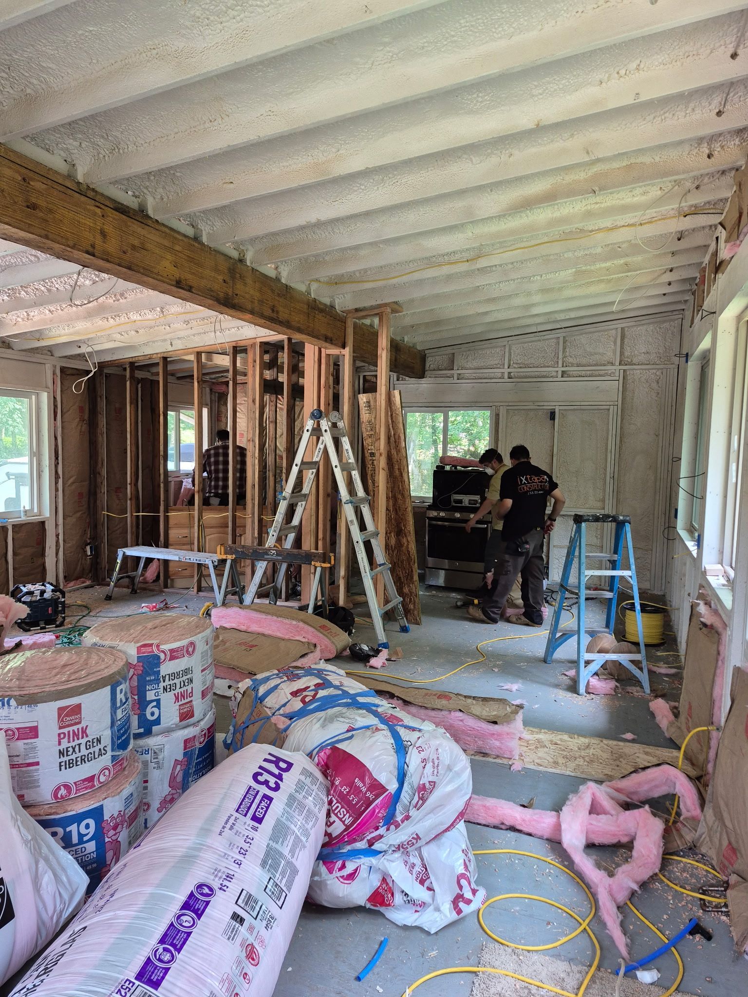 Interior of a room under renovation. Insulation, lumber, ladders, and workers present.