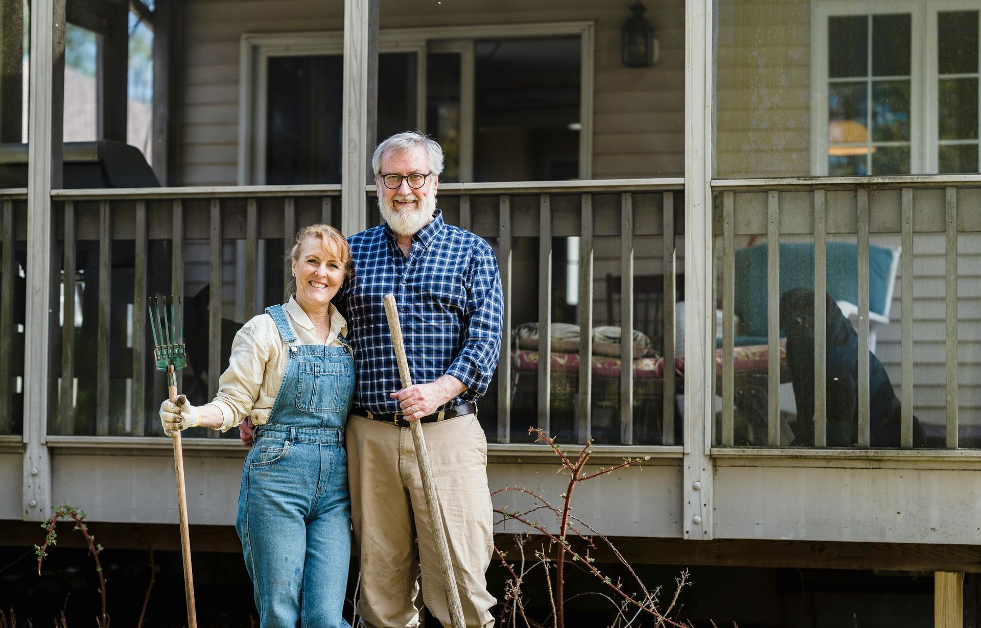 Couple with gardening tools pose in front of their home.
