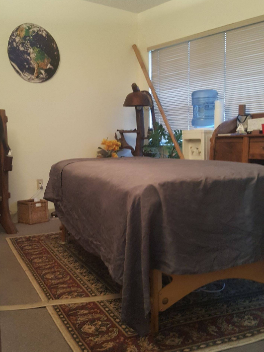 Massage therapy room with massage table, rug, water cooler, and Earth artwork.