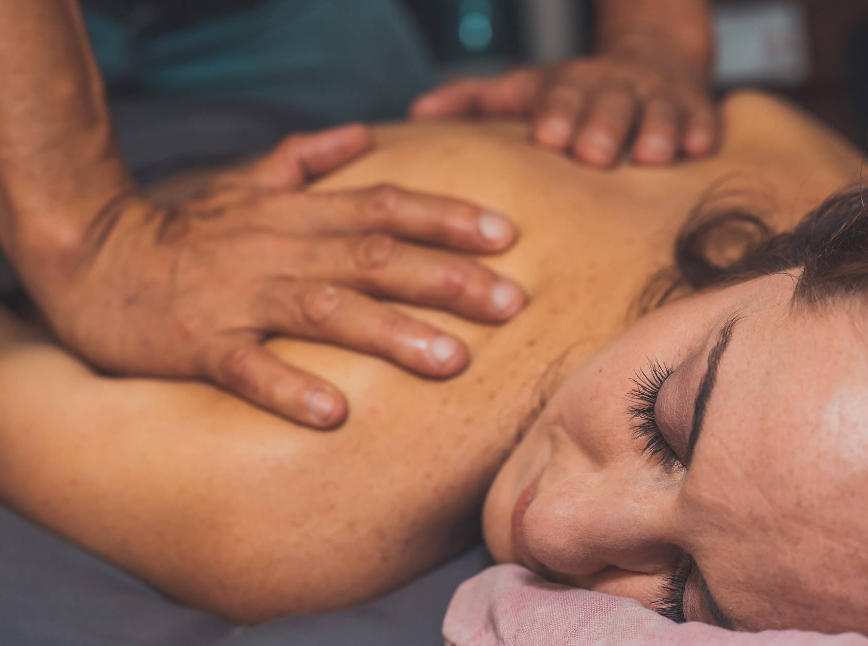 Person receiving a shoulder massage with hands pressing on their back, eyes closed, indoors.
