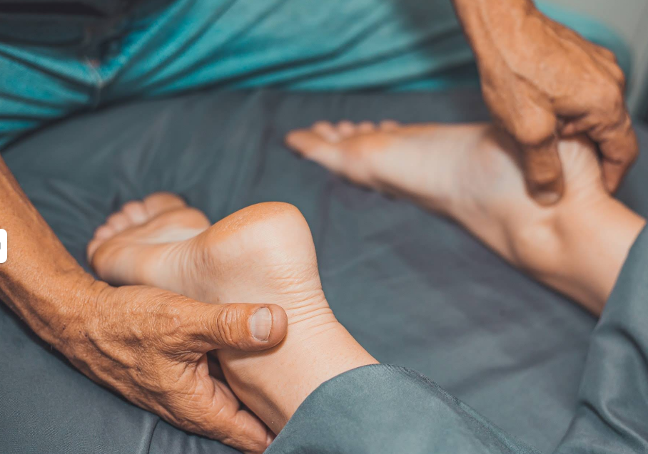 Hands massaging the foot of a person lying down on a blue surface.