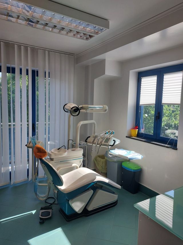 Luminosa sala per visite odontoiatriche con poltrona, lampada a soffitto, strumenti e tende alle finestre.