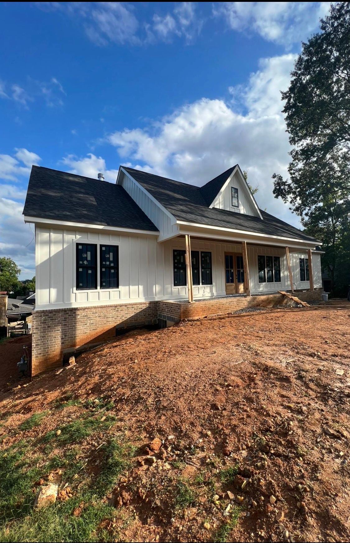 New white house with dark roof and front porch on a cleared dirt lot under a blue sky.