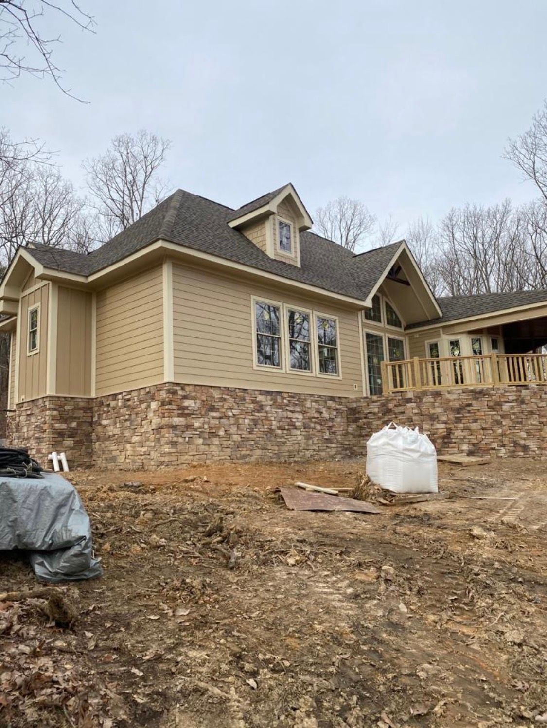 Large tan house with stone foundation on a bare hillside under a cloudy sky