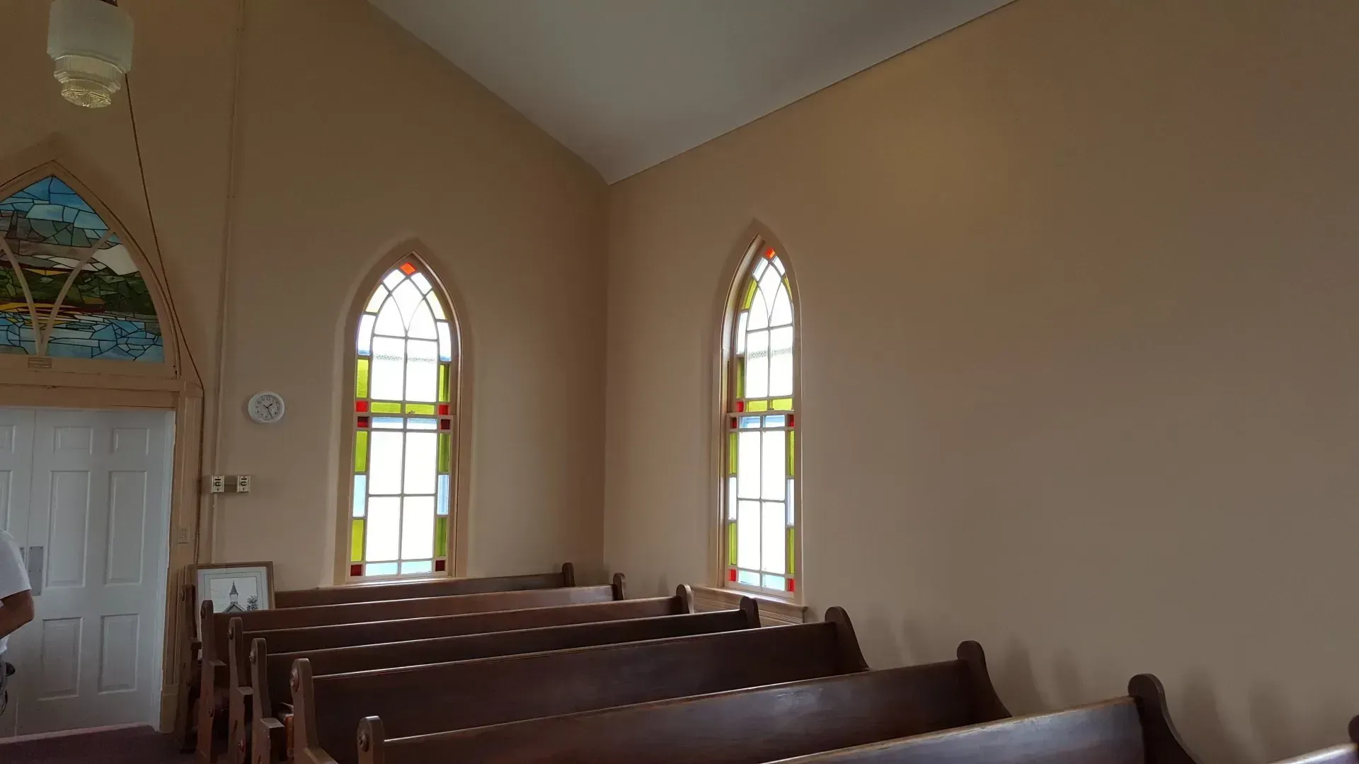 Small church interior with wooden pews and stained-glass windows along beige walls