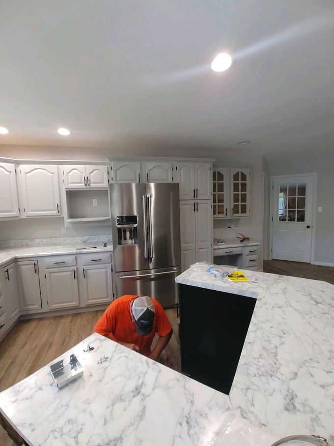 Person kneads dough on a kitchen counter beside white cabinets and a knife block.