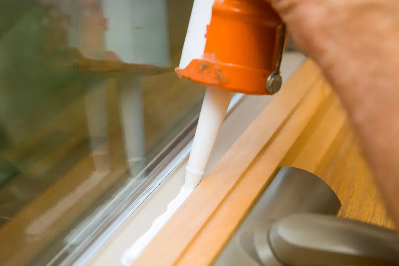 Orange caulking gun applying white sealant along a window frame