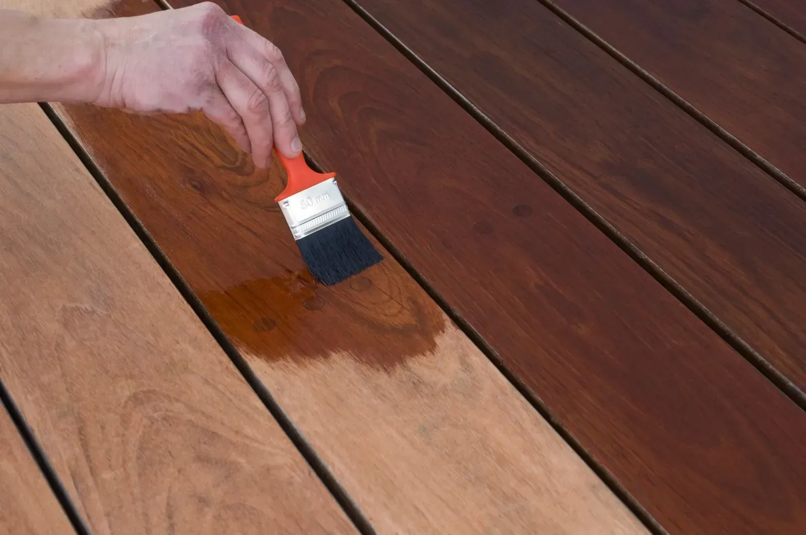 Hand brushing brown stain onto a wooden deck plank