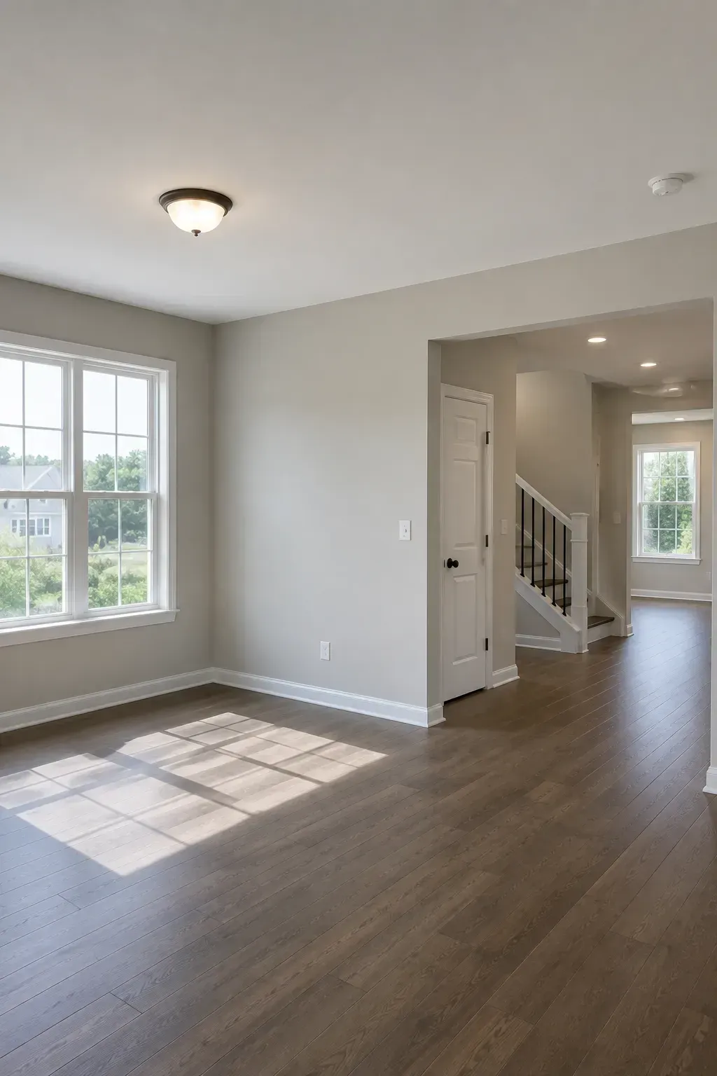 Empty living room with gray walls, wood floors, large window, and stairway hallway view.