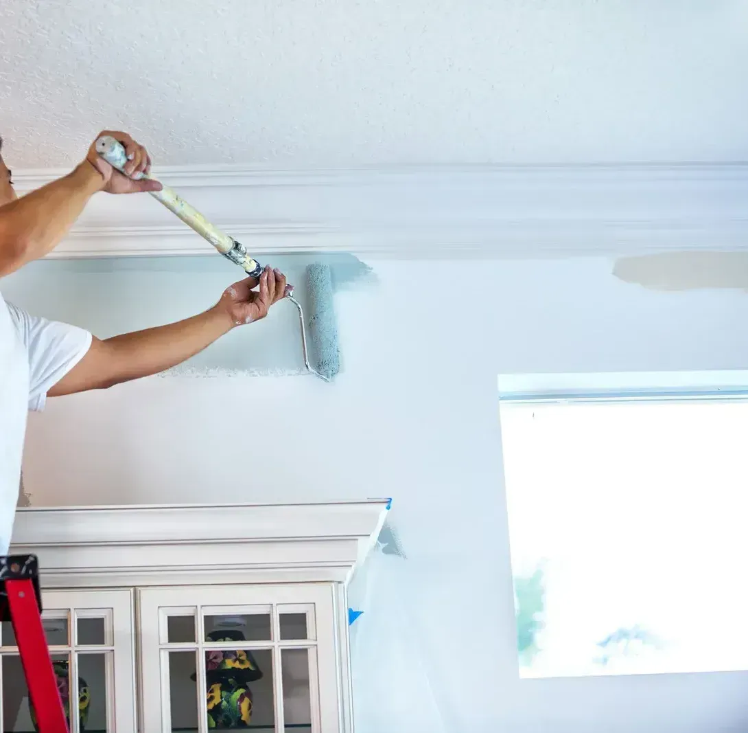 Person painting a white ceiling near a window with a roller