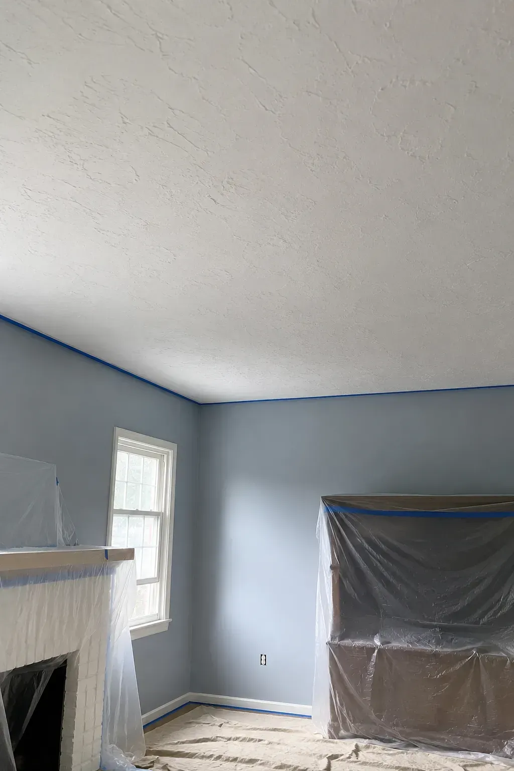 Partially finished room with gray walls, white ceiling, a window, and plastic-covered furniture.