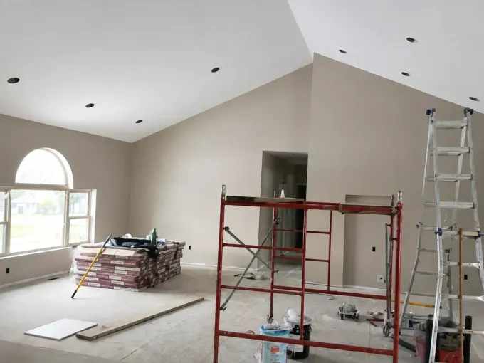 Person painting white crown molding with a roller on a ceiling in a bright room
