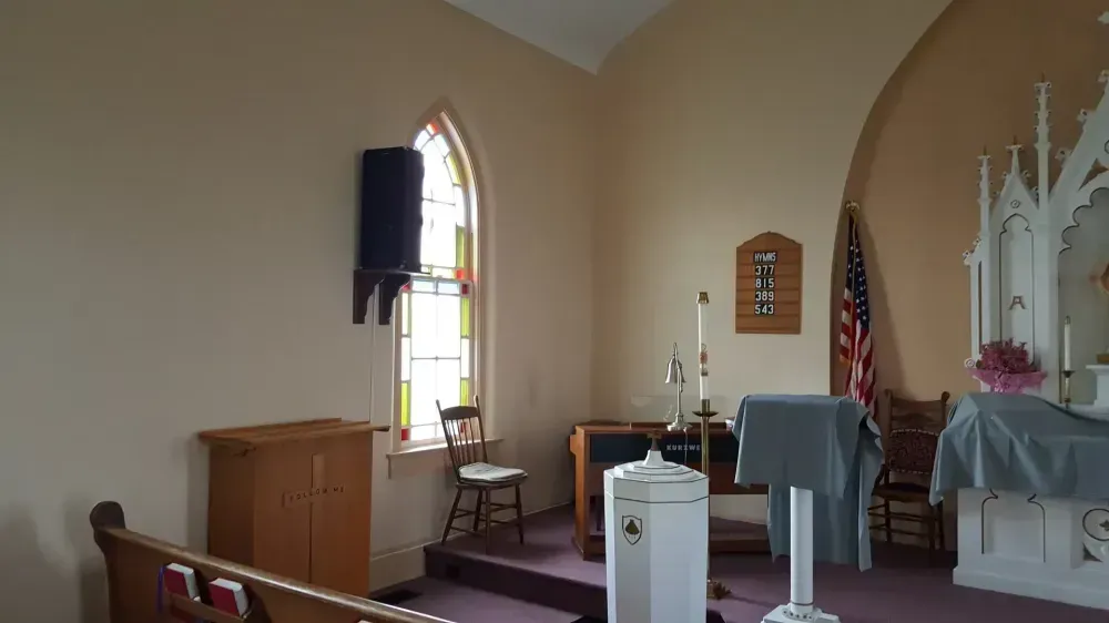 Small church sanctuary with lectern, pews, stained glass window, and altar draped in white.