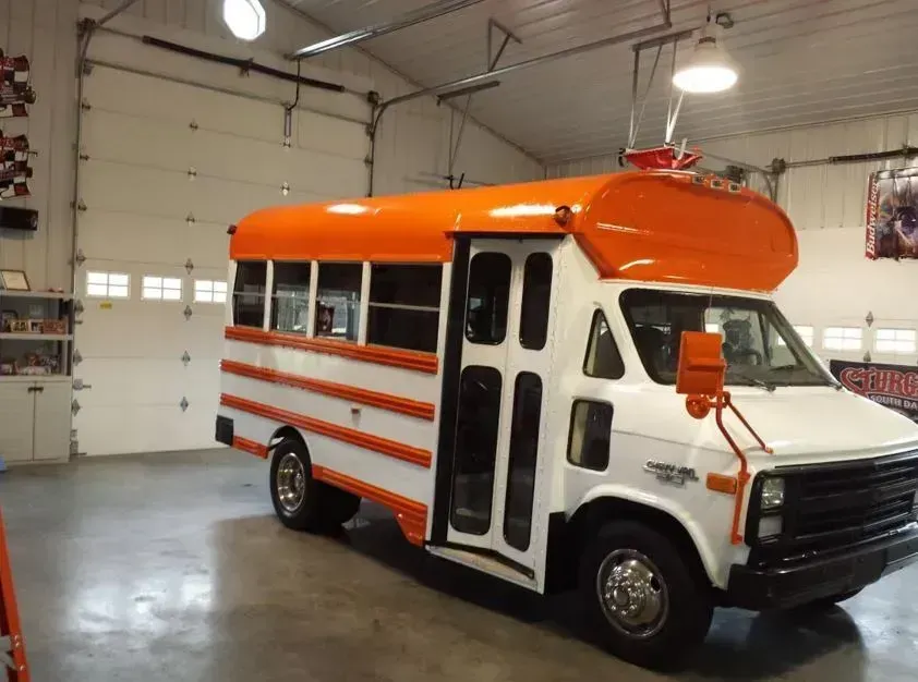 Orange-and-white school bus parked inside a garage with white walls and overhead lights