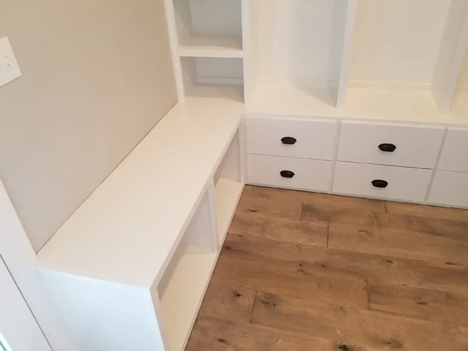 White built-in bench and drawers in a small room with light wood floor and shelving.