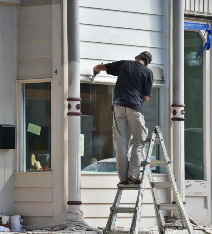 Worker on a ladder painting or repairing the exterior wall of a white house