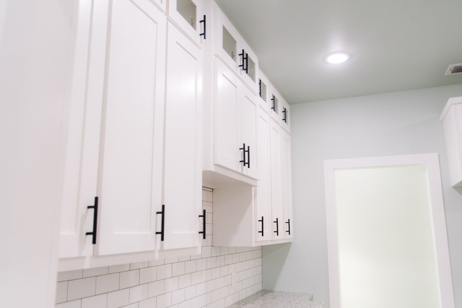 Partially renovated kitchen with gray and wood cabinets, blue painter’s tape, and a hand adjusting a cabinet door
