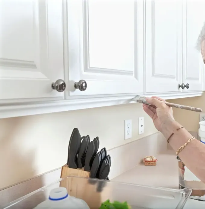 Hand placing a braided cord on a kitchen countertop beside a knife block and white cabinets