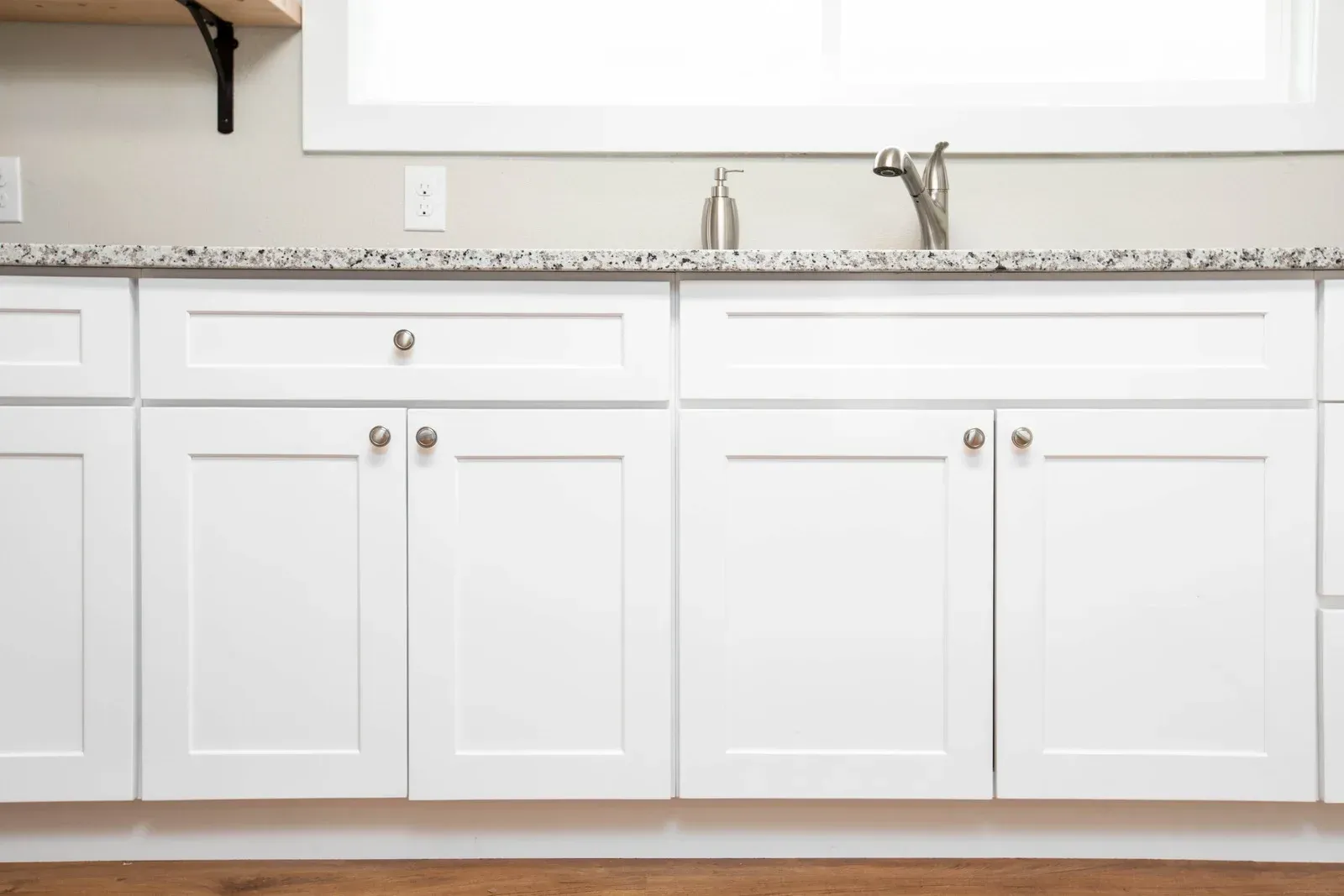 Hand brushing gray cabinet doors beside a wood-grain cabinet panel