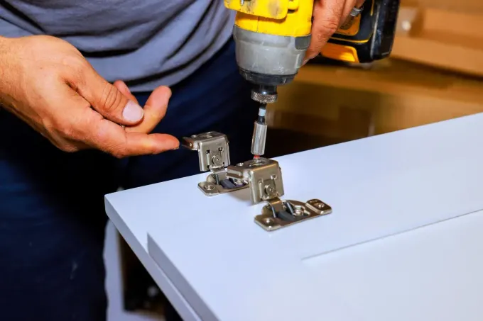 Person drilling a hole in a wooden floor with a yellow power drill and green gloves